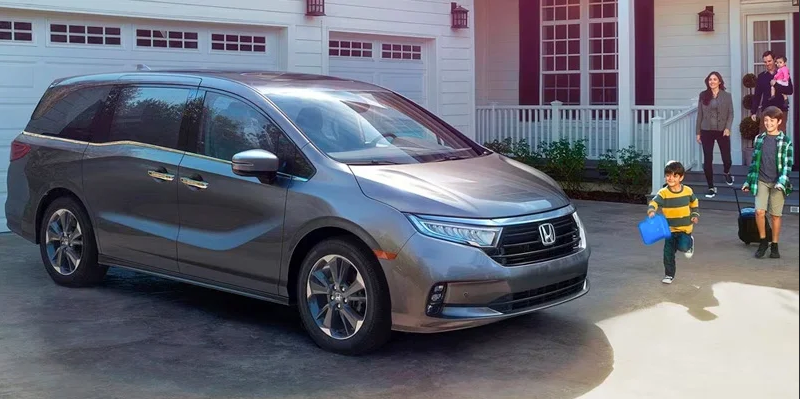 A family coming out of the house with school bags to get in their 2024 Honda Odyssey parked in the driveway.