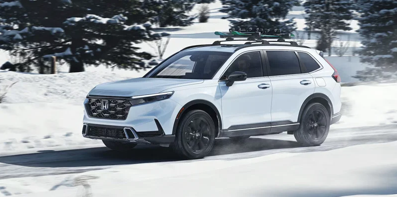 A white 2025 Honda CR-V Hybrid driving through the snow.