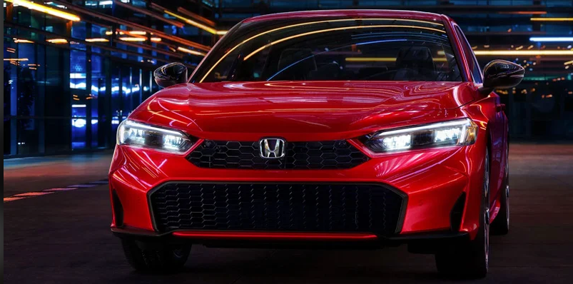 A red 2024 Honda Civic Hatchback driving down the road with blurred lights in the backround.