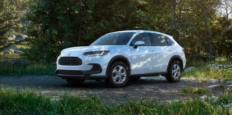 A white 2024 Honda HR-V parked on a dirt patch with trees in the backround.