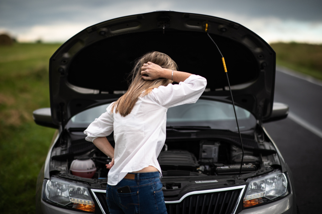 A woman standing in front of her car broken down on the side of the road.