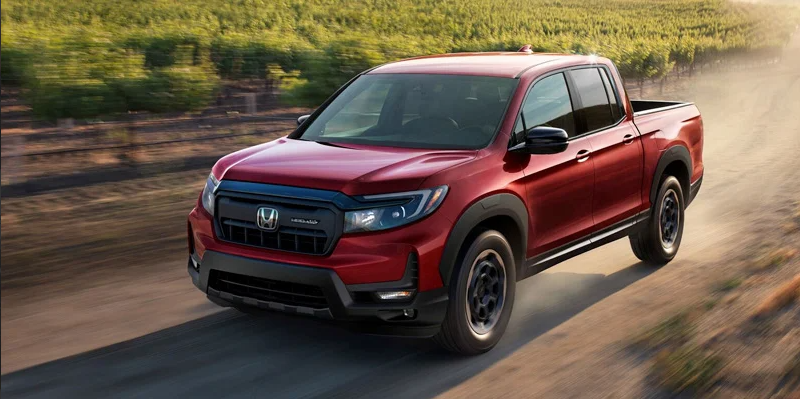 A red Honda Ridgeline driving down a dirt road.