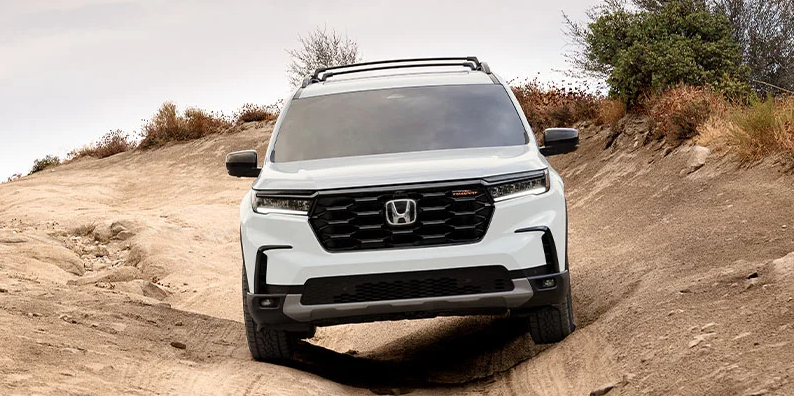 A white 2025 Honda Pilot driving down a dirt trail.
