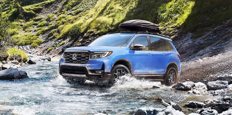 A blue 2025 Honda Passport driving through a stream of water.
