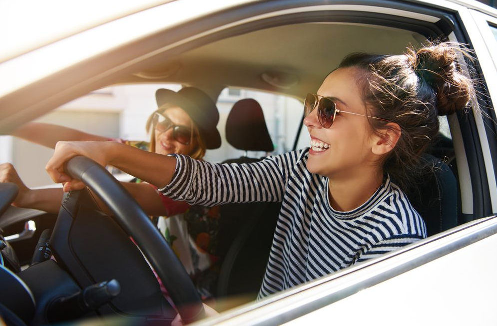 2 Friends driving down the road in a white car smiling.