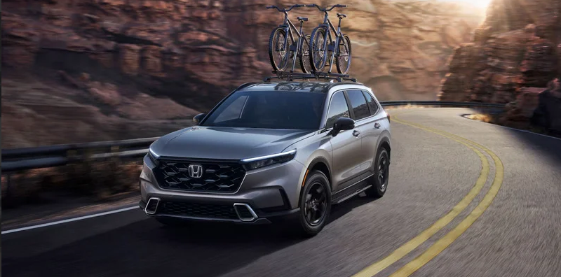 A photo of a 2025 CR-V hybrid driving down the road with bikes on its roof rack.