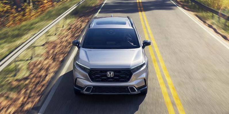 A photo of a silver 2026 Honda CR-V hybrid driving down the road.