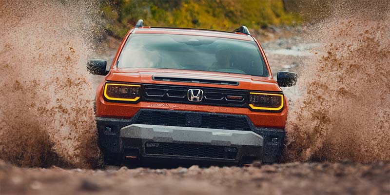 Orange 2026 Honda Passport off-roading through muddy terrain