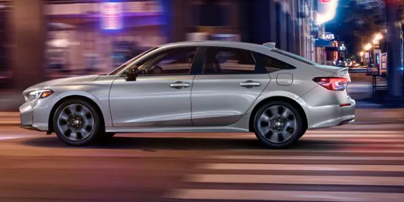 Silver 2026 Honda Civic Sedan Hybrid driving through city streets at night