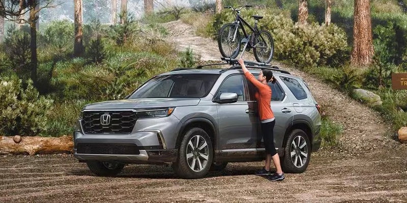 A woman straps a bike to the top of a 2024 Honda Pilot